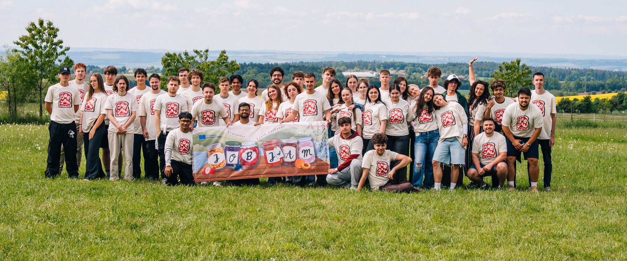 The Job Jam group in team shirts holding the Job Jam banner on a meadow
